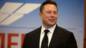 Elon Musk, CEO of Tesla, with Tesla's Subpoena, wearing a black suit with a black tie.