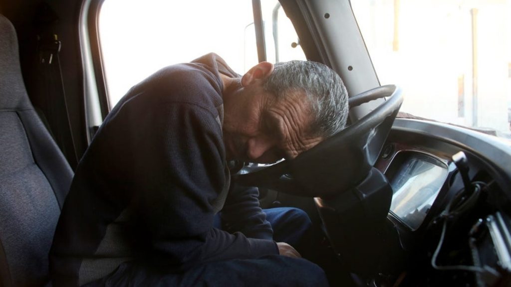 Truck driver exhausted, resting head on steering wheel
