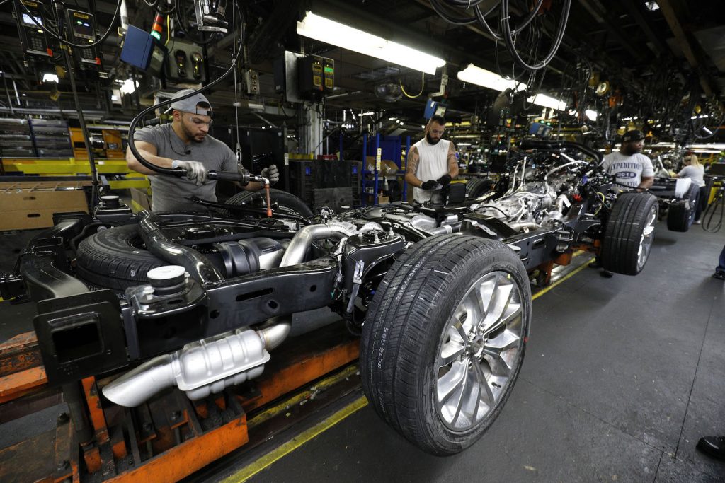 Factory workers assembling a Ford Expedition SUV, its truck-like full-frame construction visible.