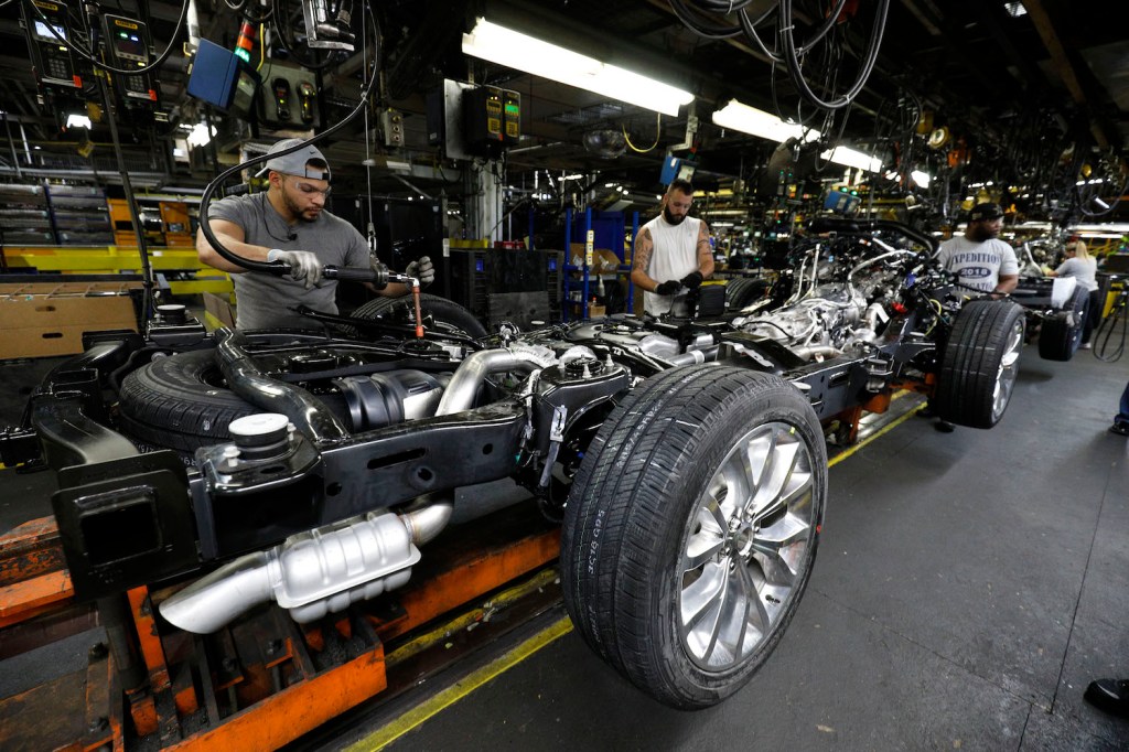 Factory workers assembling a Ford Expedition SUV, its truck-like full-frame construction visible.