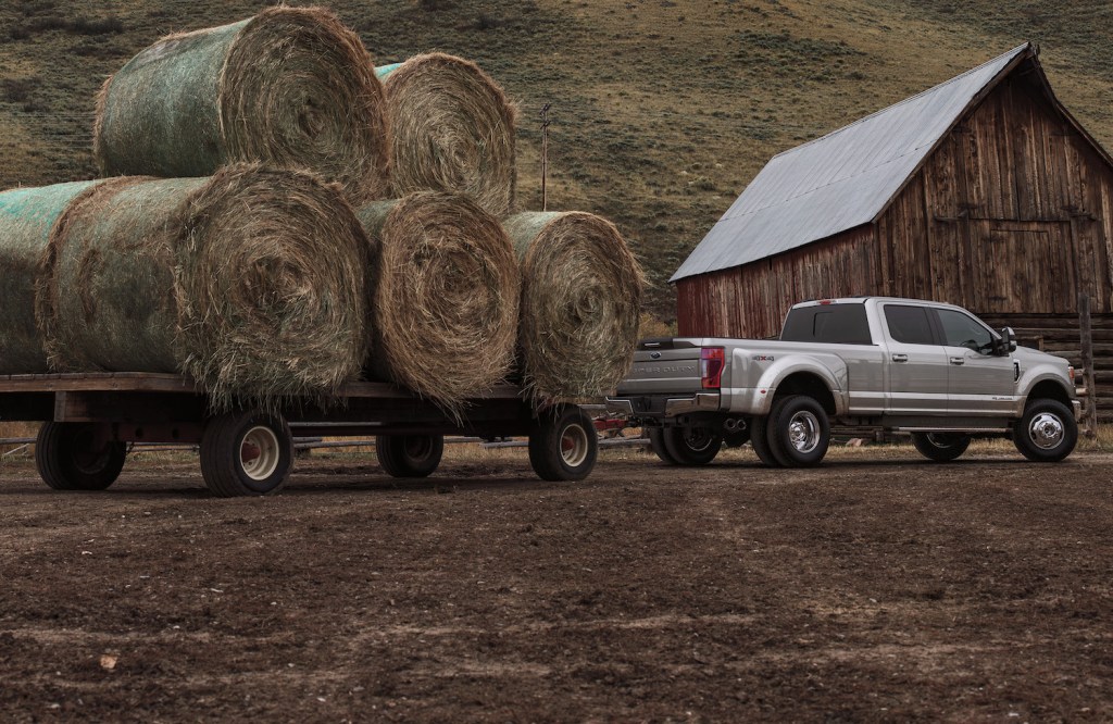 Promo shot of a Ford F-250 Super Duty pickup truck hauling a trailer loaded with hay bales in front of an old barn.
