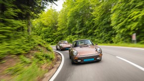 A pair of vintage 1970s Porsche sports cars, including a 1975 930 Turbo and a 1974 2.7 Carrera MFI, driving in the hills outside Vienna