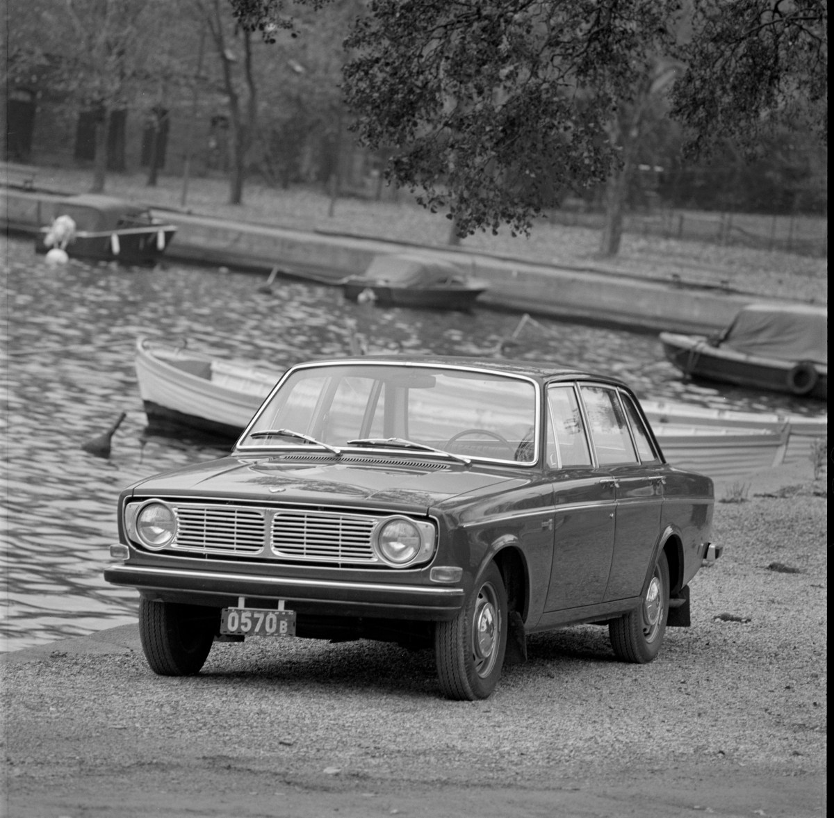A 3/4 front view of a 1967 Volvo 140 Series sedan. Photo is in black and white and shows boats and water in the background