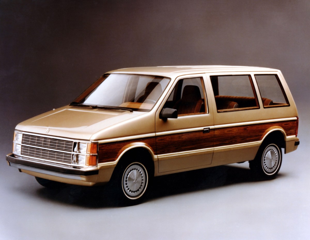 A 3/4 front view of a gold and faux wood-paneled 1983 Dodge Caravan with a shaded studio background.