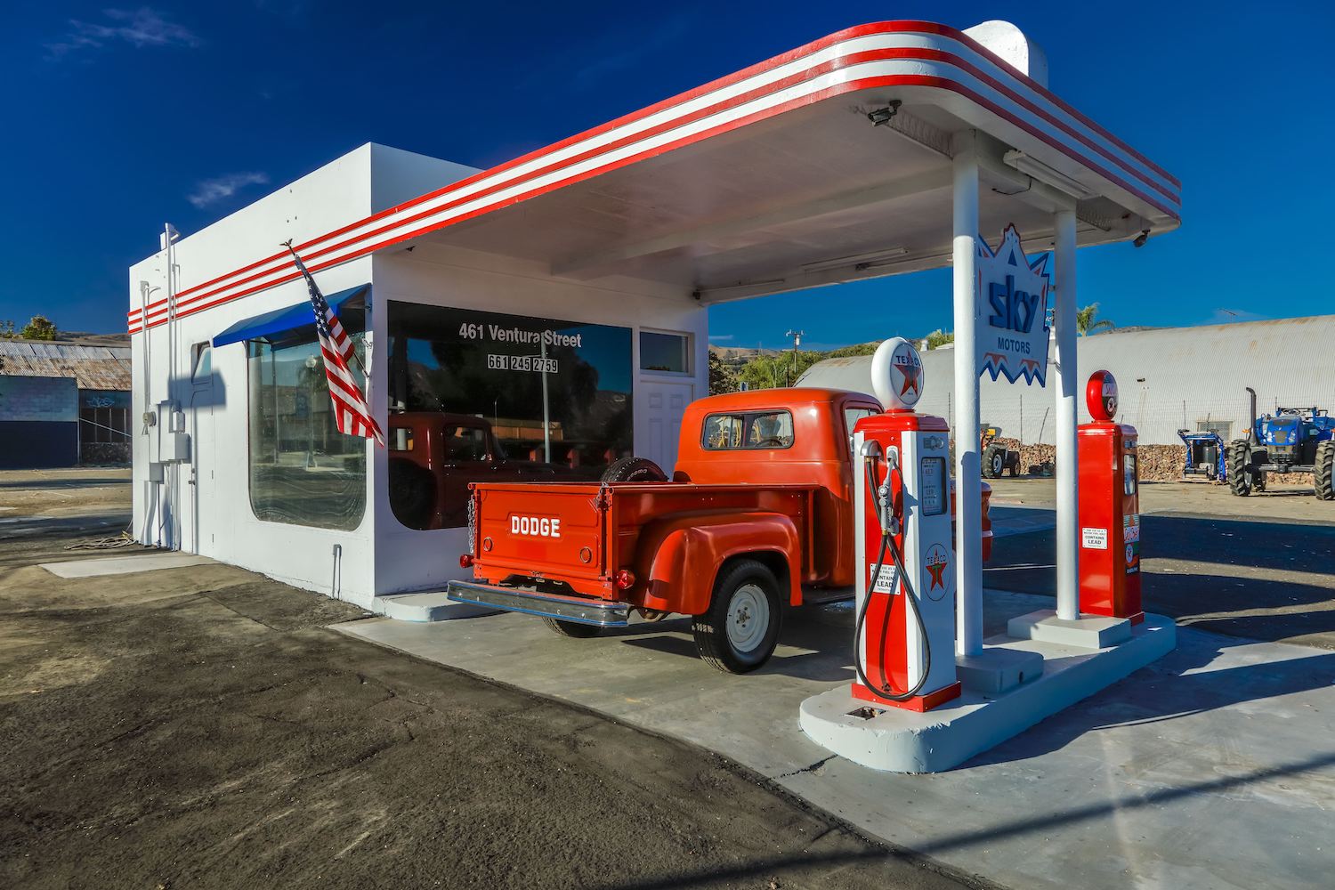 A red vintage dodge ram pickup truck parked at a gas station.