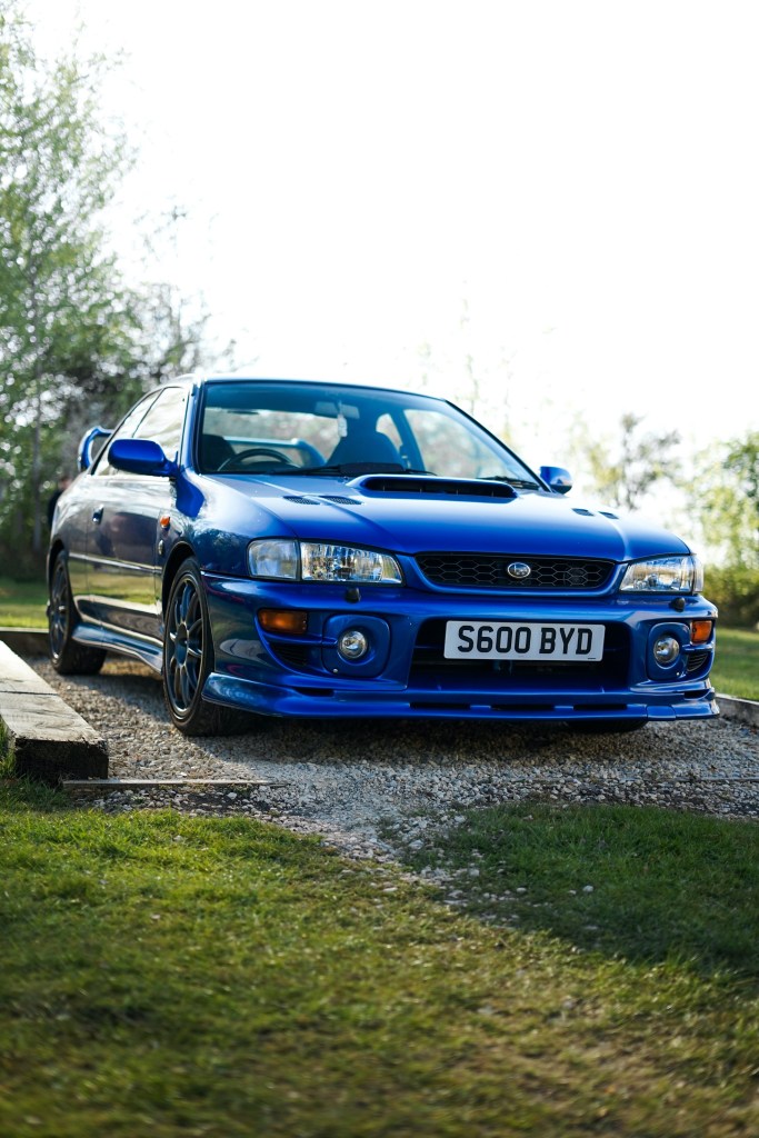 A blue modified JDM GC8 Subaru Impreza WRX parked in a grassy field