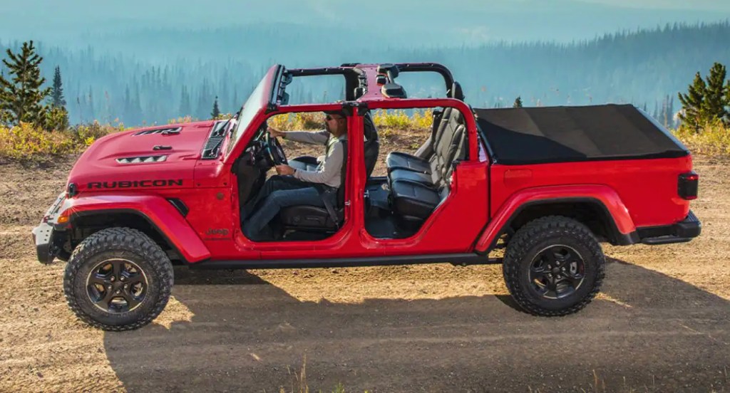 A red Jeep Gladiator pickup truck is parked off-road. 