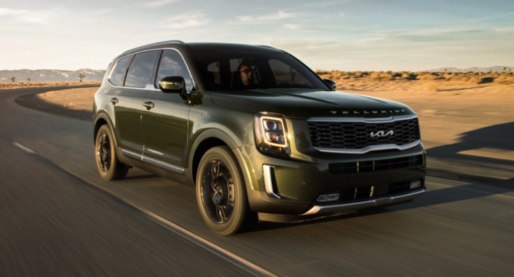 A green Kia Telluride is driving on the road. 