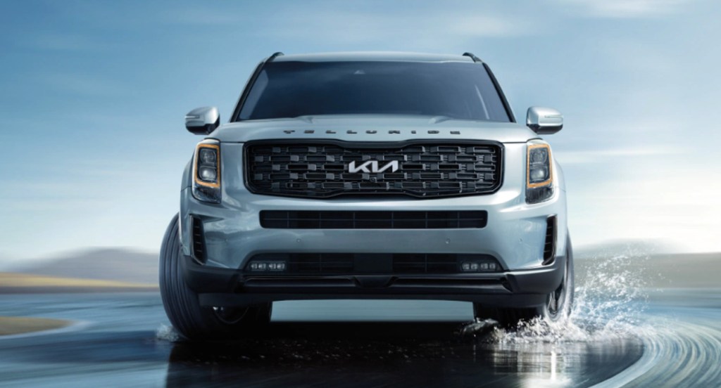 A gray Kia Telluride is driving on a wet road. 