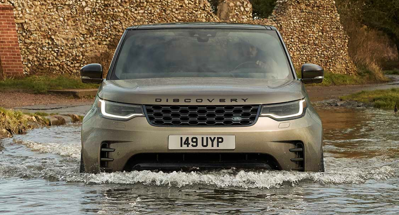 A gray Land Rover Discovery is driving in water.