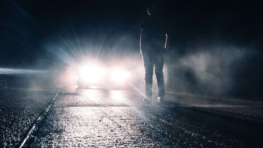 Man standing in front of a car with the high beam headlights activated