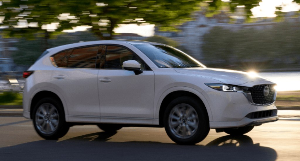 A white 2022 Mazda CX-5 compact SUV is driving on the road. 