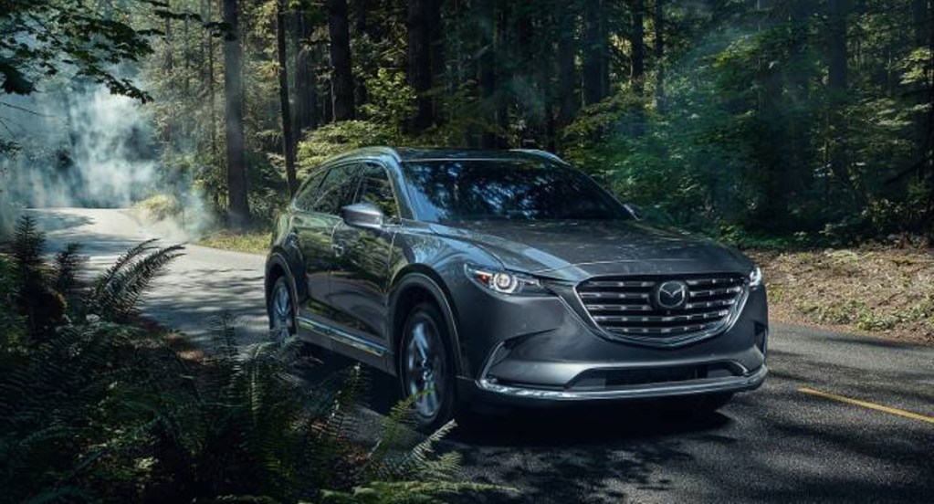 A gray Mazda CX-9 is driving down the road. 