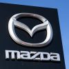 A black Mazda sign in front of a blue clear sky with the Mazda logo in silver on it.