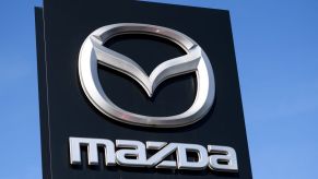 A black Mazda sign in front of a blue clear sky with the Mazda logo in silver on it.