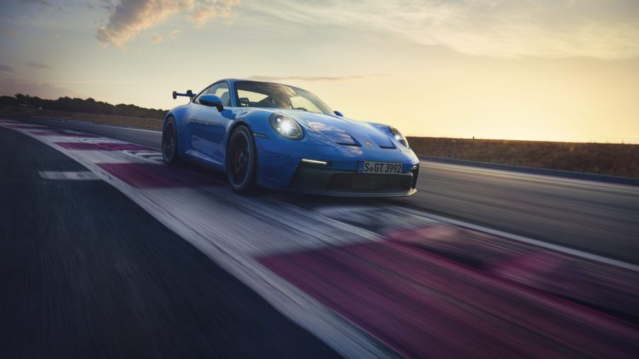 A 3/4 front view of a blue 2022 Porsche 911 GT3 cornering on a race track with a sunset in the background.