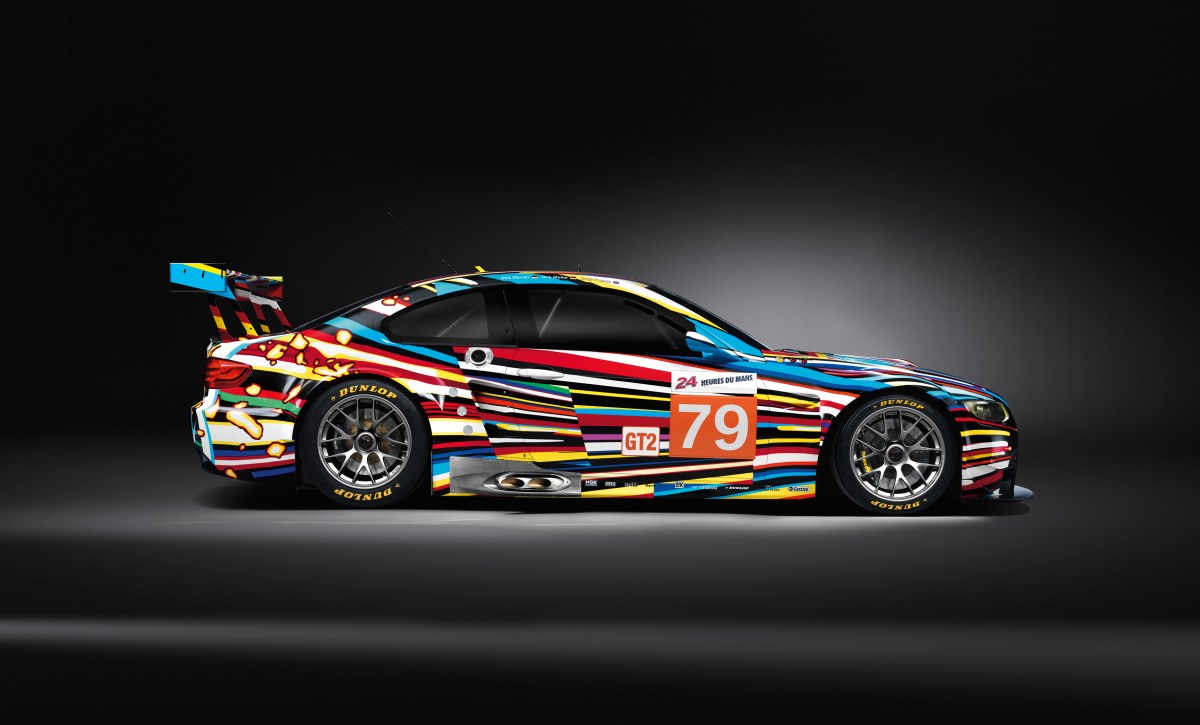 A profile view of the 2010 BMW M3 GT2 race car painted by Jeff Koons with a black studio background. 