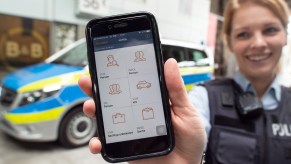 A policewoman smiling and holding up an iphone she uses for her job.