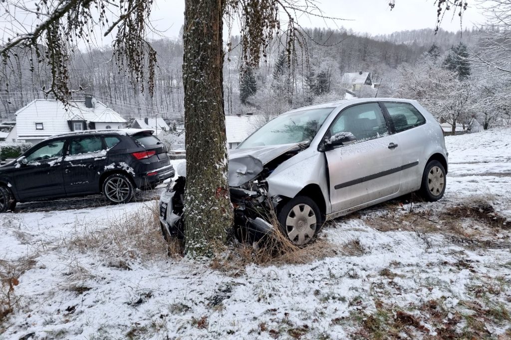 A silver vehicle that hit a tree with snow on the ground.