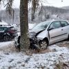 A silver vehicle that has hit a tree with snow on the ground.