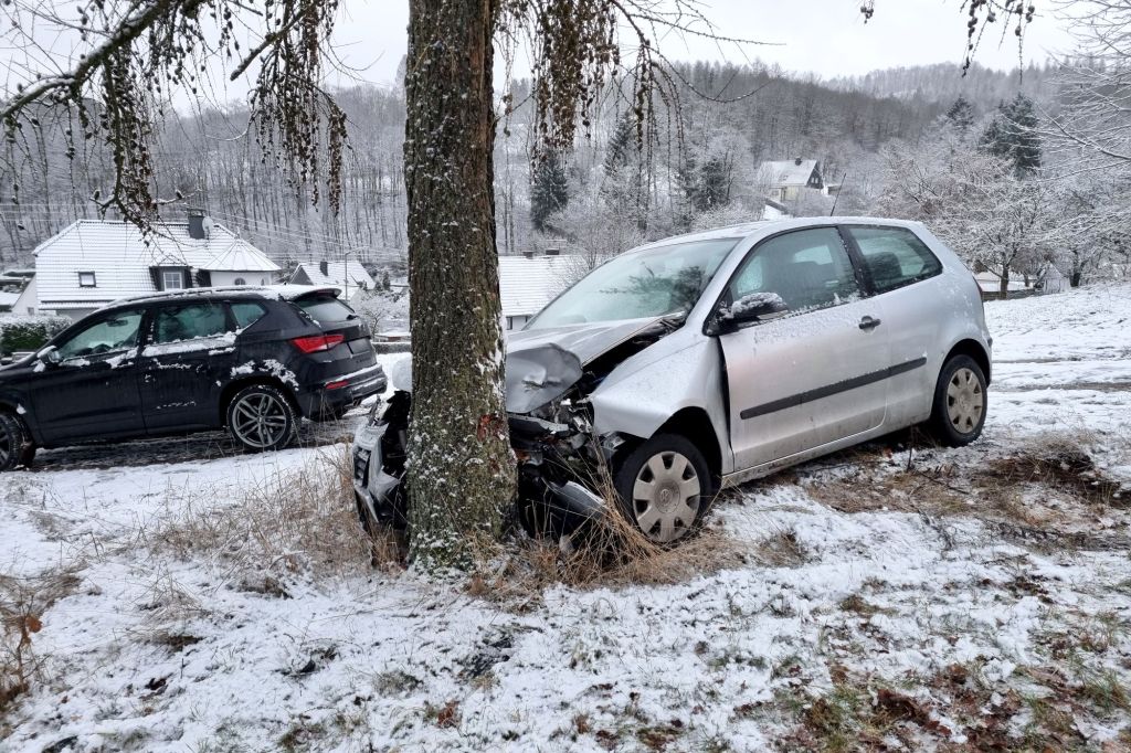 A silver vehicle that has hit a tree with snow on the ground. 