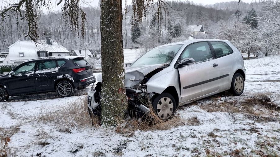 A silver vehicle that has hit a tree with snow on the ground.