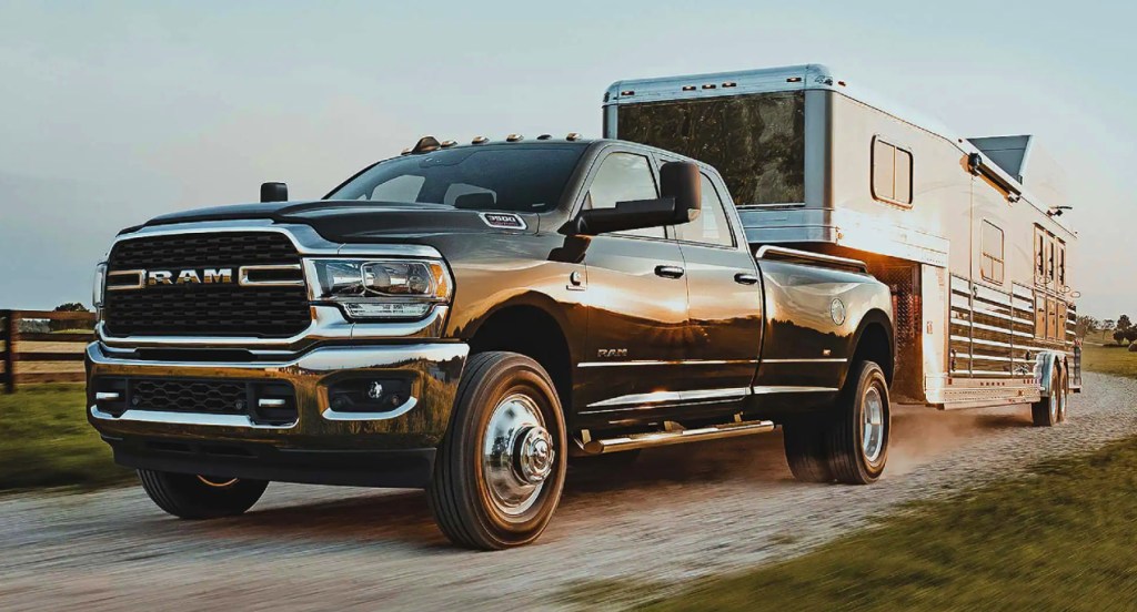 A black Ram 3500 heavy duty pickup truck is towing a trailer off-road. 