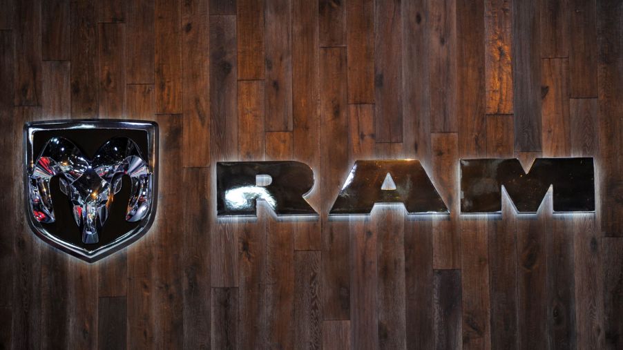 Ram logo, makers of the Ram 1500 TRX, on a wood plank background with the letters and symbol in chrome backlite with a white light.