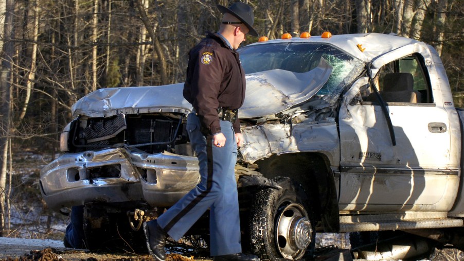 Police officer looking at the caved-in grille of a smashed Ram truck.