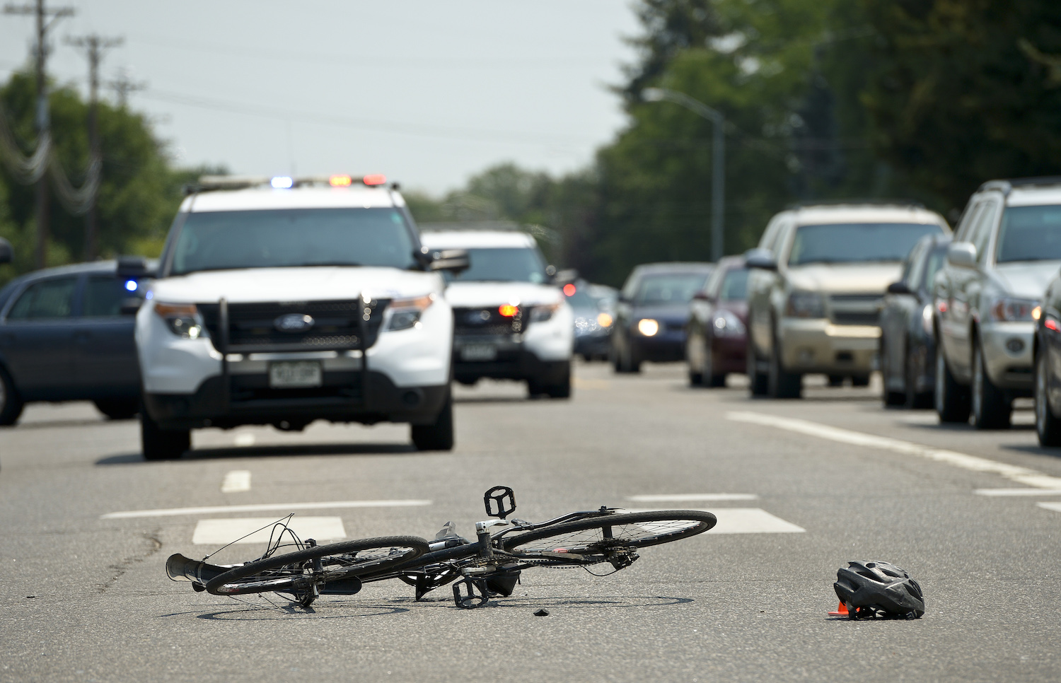 A smashed bicycle on the pavement, surrounded by police cruisers, after a crash with a pickup truck.