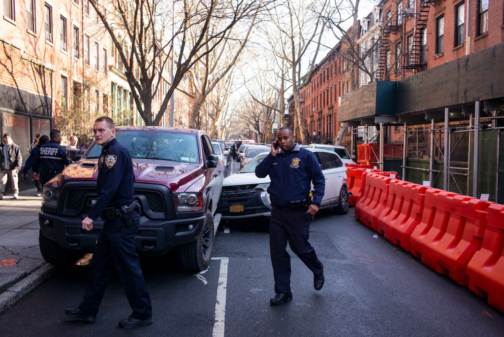 Police officers surrounding a red Ram truck involved in a crash with a Mitsubishi SUV between city buildings.