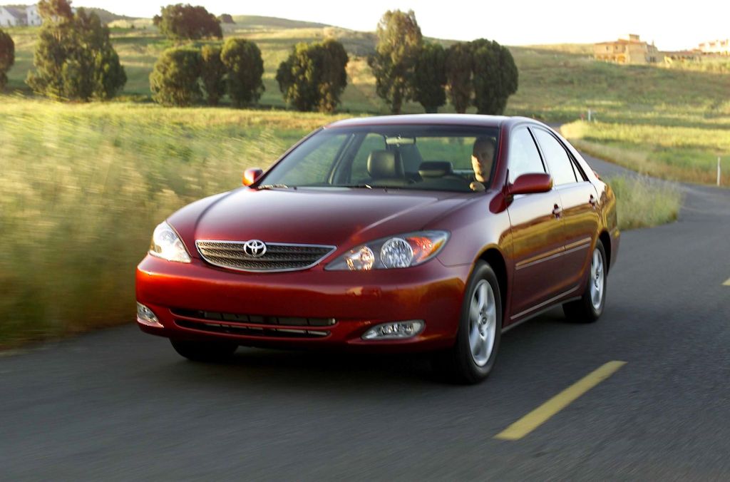 Red 2005 Toyota Camry, one of the best used cars priced under $5,000, driving on a country road