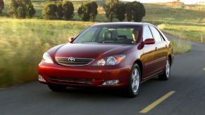 Red 2005 Toyota Camry, one of the best used cars priced under $5,000, driving on a country road