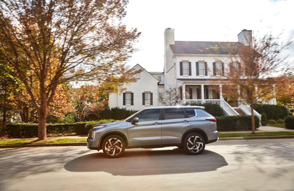 Silver 2022 Mitsubishi Outlander driving by a large house, highlighting how Mitsubishi has good warranty coverage