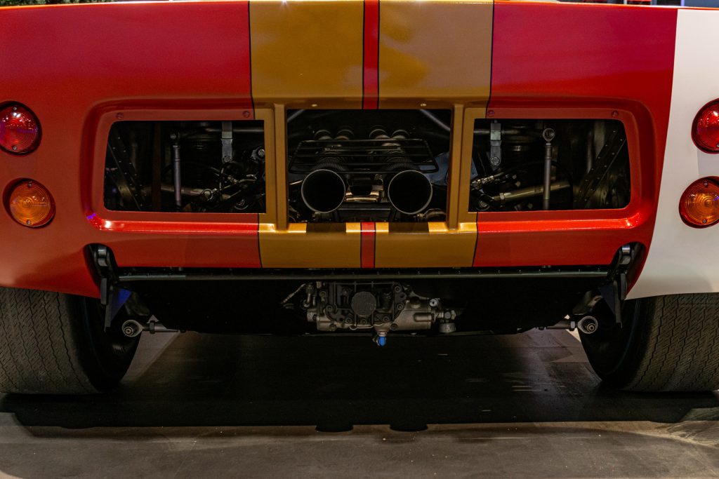 The red-and-gold 1966 Ford GT40 Mk I Lightweight AM GT-1's V8 engine, exhaust, and transaxle seen from the rear