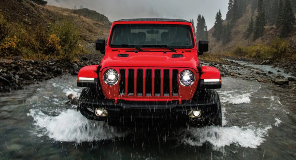 A red Jeep Wrangler is driving through the water. 