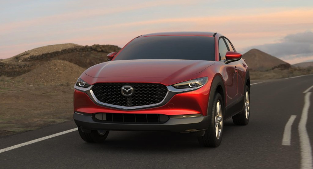 A red Mazda CX-30 subcompact SUV is driving down the road. 