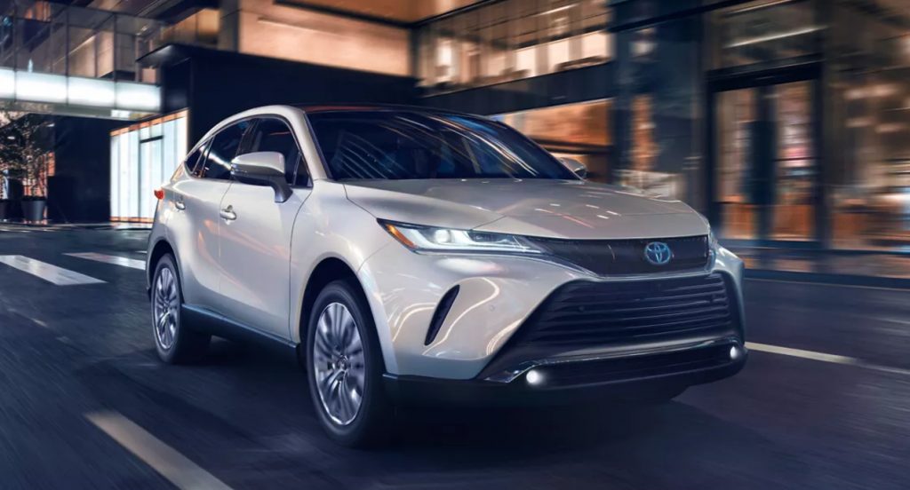 A white 2022 Toyota Venza hybrid SUV is driving on the road. 