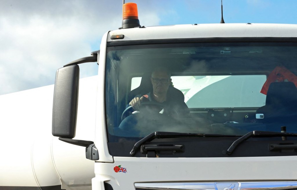 A truck driver in a white semi-truck driving.