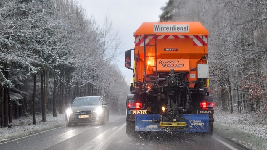A snow plow spreads road salt over a snowy road