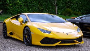 A yellow Lamborghini Huracan sitting on gravel in front of a wooded area.