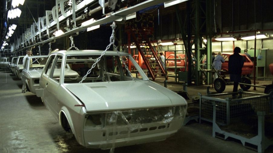 A white Yugo hatchback in a factory environment stripped of various parts.
