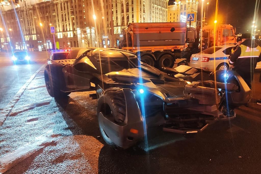 A batmobile replica surrounded by cops on the street in Russia, at night.