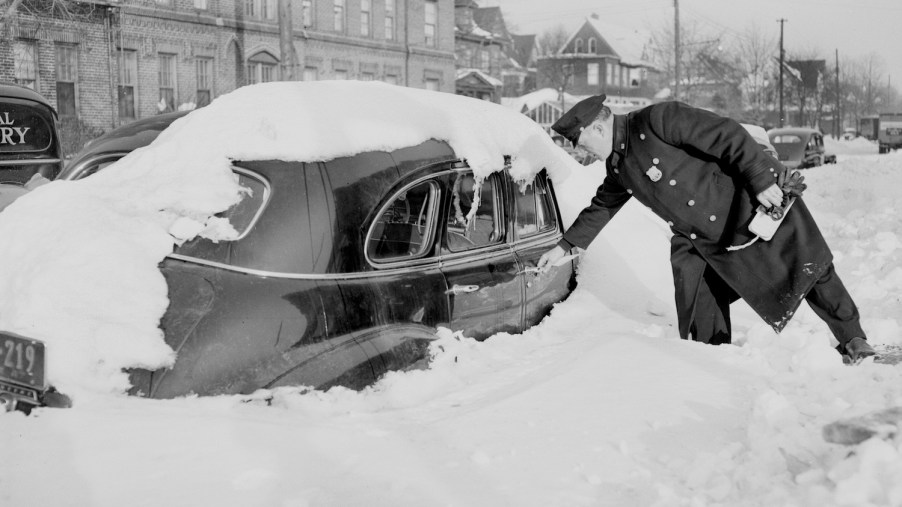 This is a police officer ticketing a snow-covered car for violating a winter parking ban.