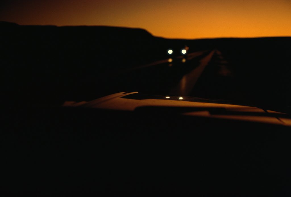 A car driving through a desert, flashing its high beams at oncoming traffic.
