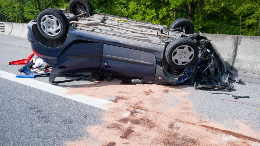 A rollover car accident on the side of the road with the car upside down.