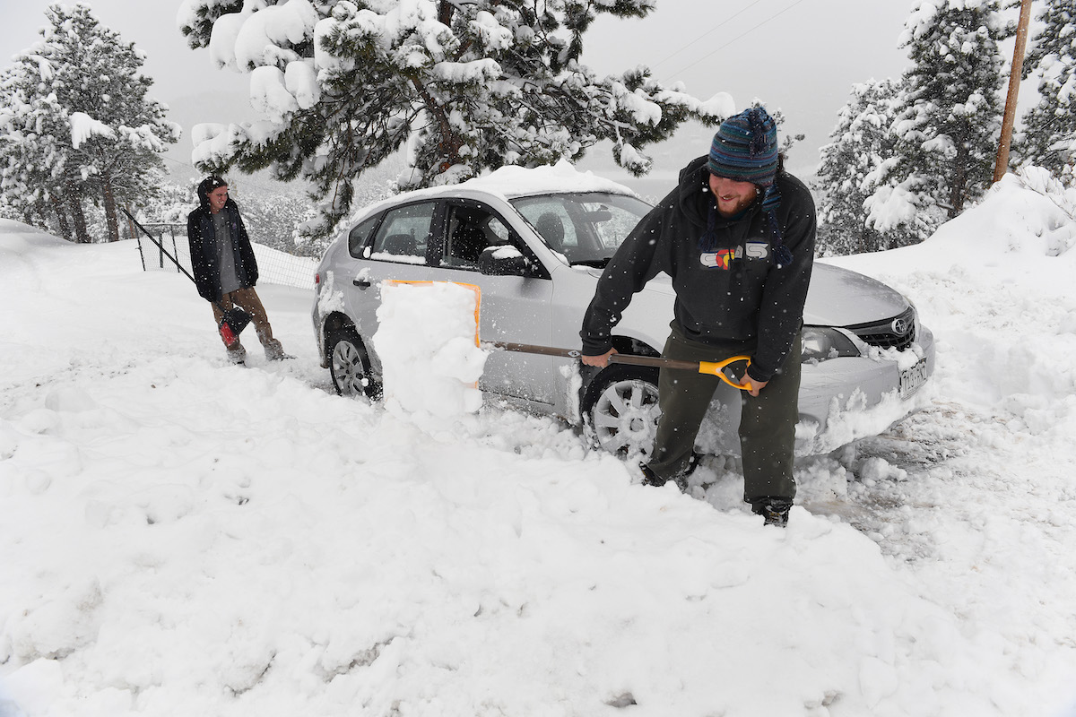 Two men shoveling snow around a stuck car in a driveway in April 2016 in Nederland, Colorado