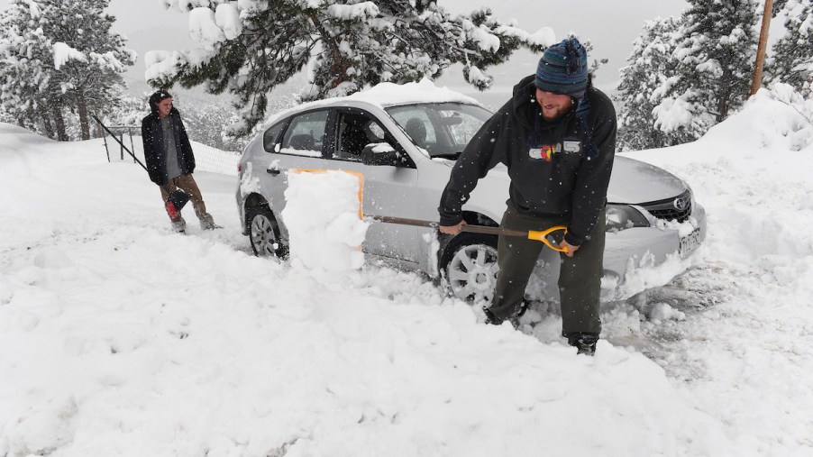 Two men shoveling snow around a stuck car in a driveway in April 2016 in Nederland, Colorado