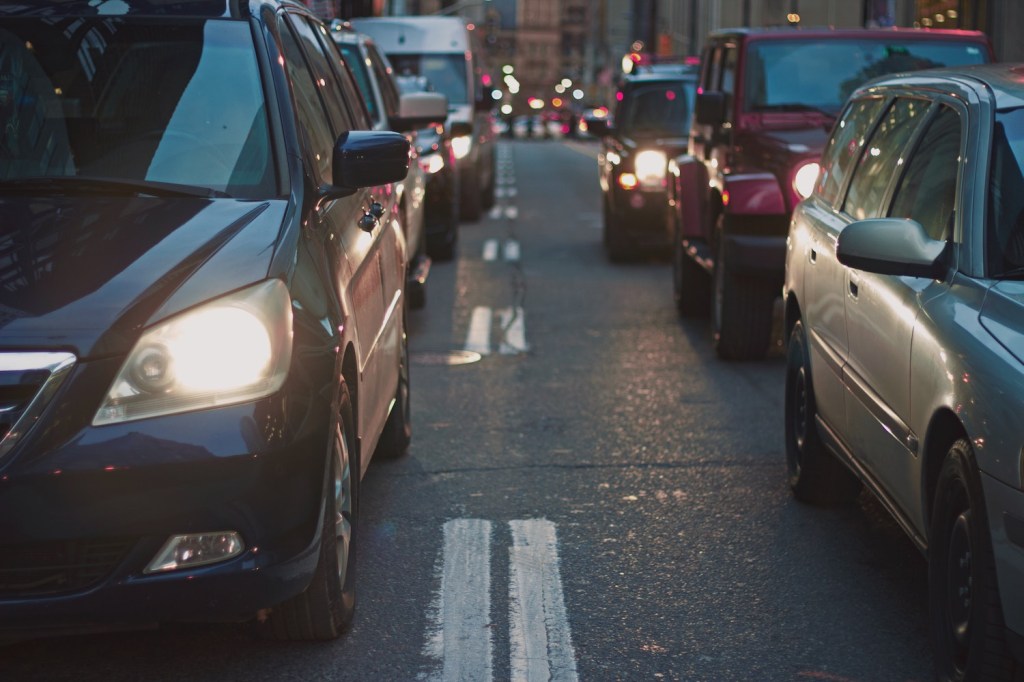 Cars parked bumper-to-bumper in stop and go traffic between city buildings.