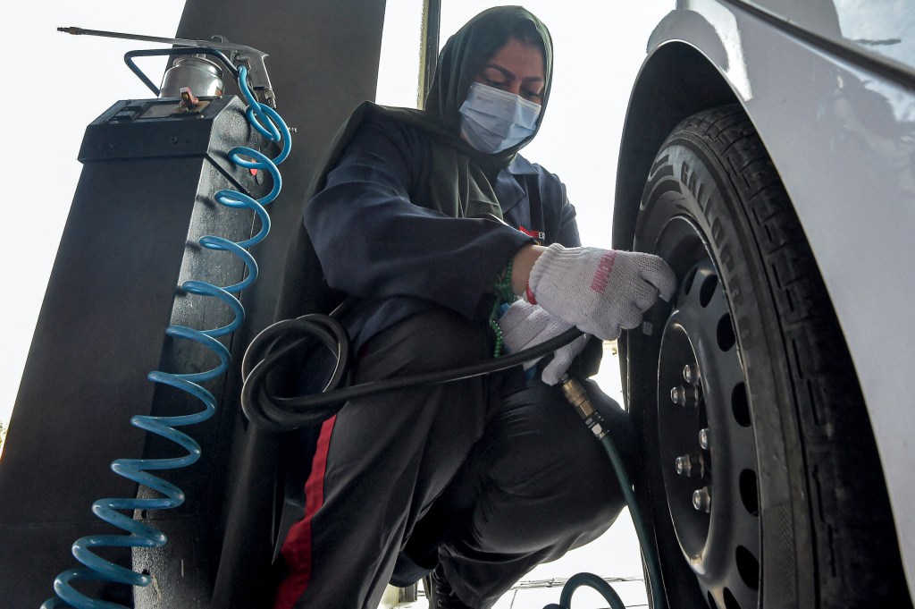 A Saudi woman mechanic fills up the air in a vehicle tire at a repair and service garage